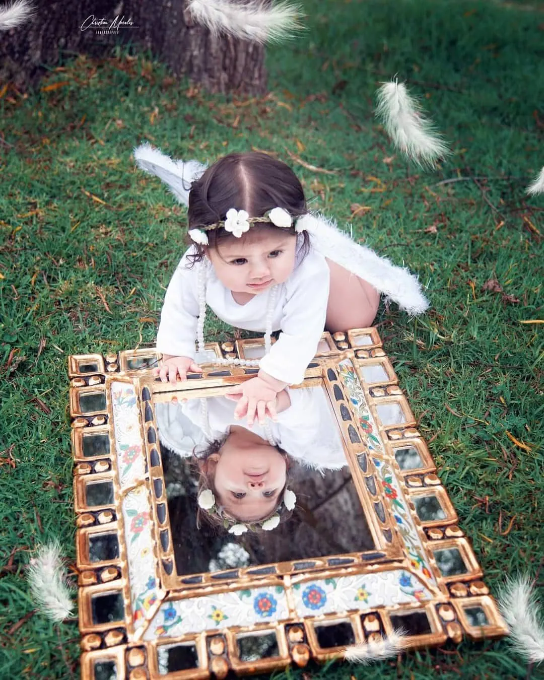 Bebé vestida de ángel mirándose en un espejo dorado