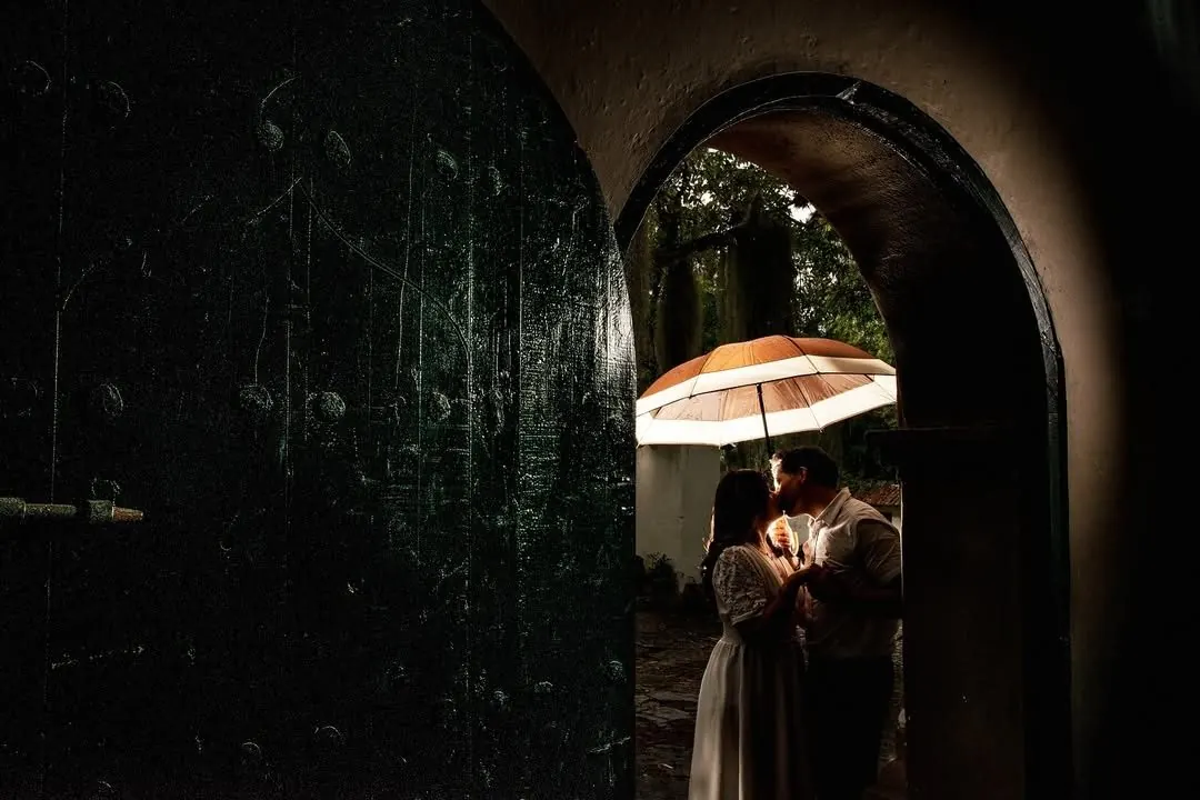 Novios besándose bajo un paraguas en un arco colonial
