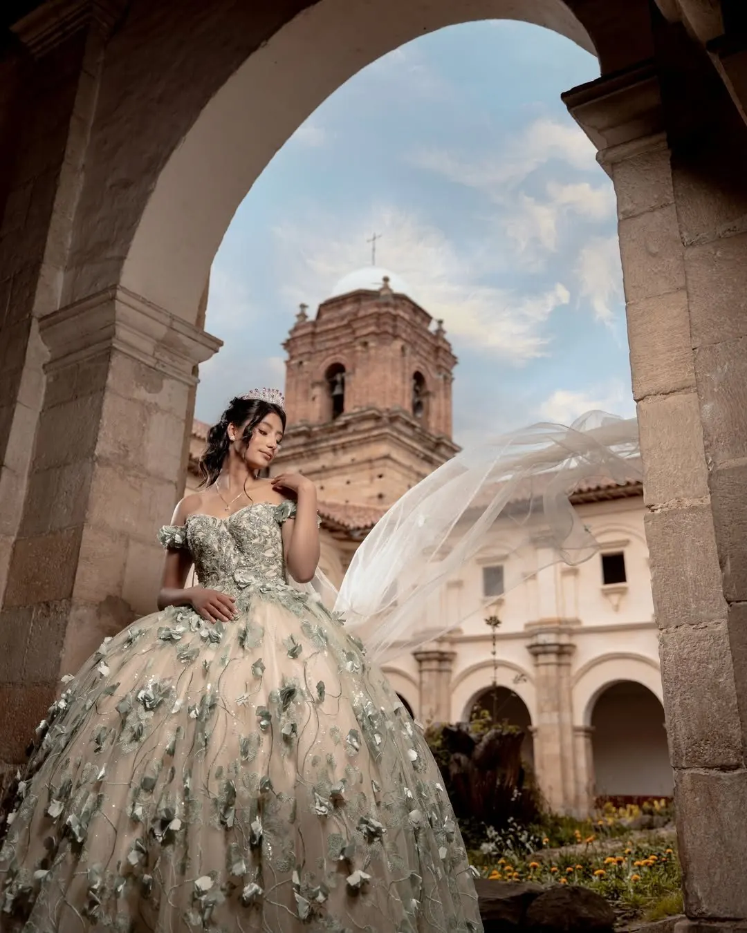 Quinceañera bajo arcos coloniales con iglesia de fondo