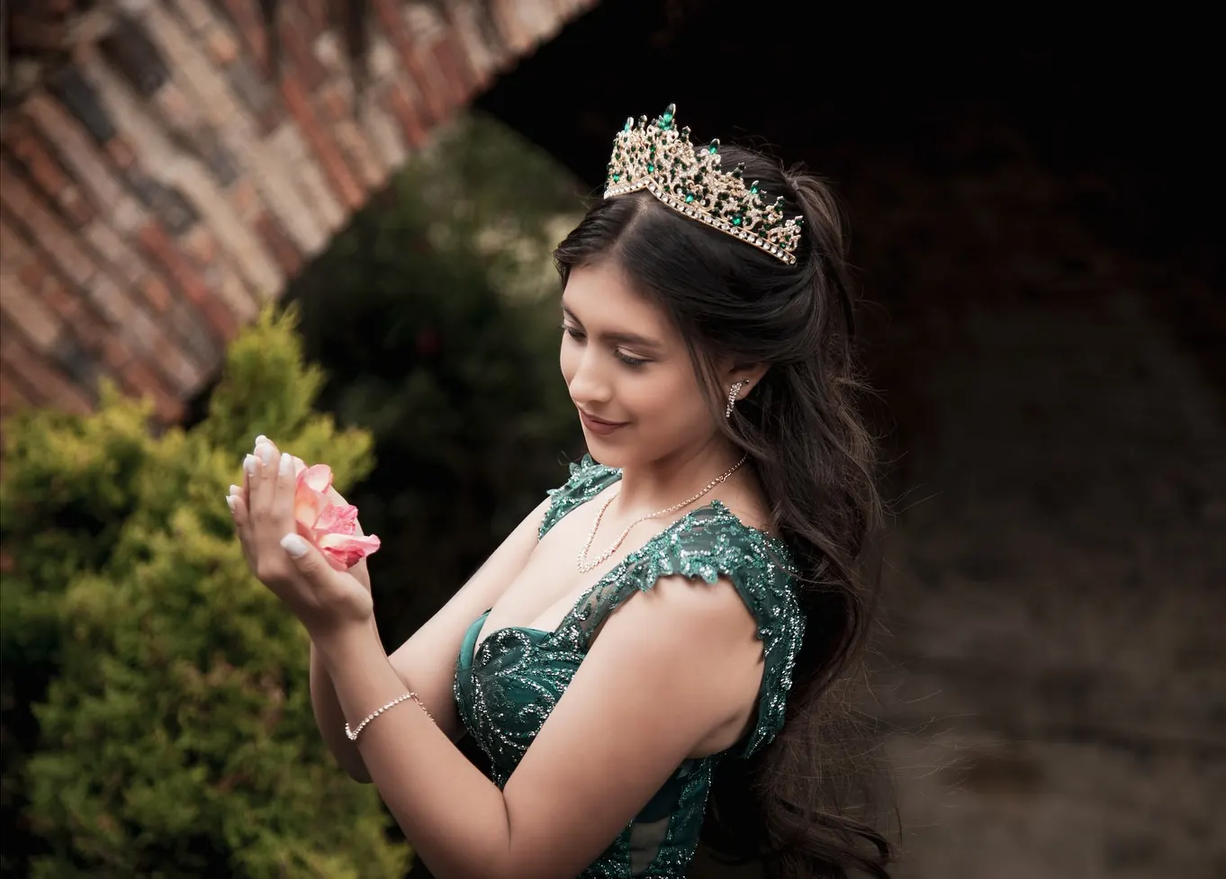 Quinceañera con corona y vestido verde sosteniendo una rosa